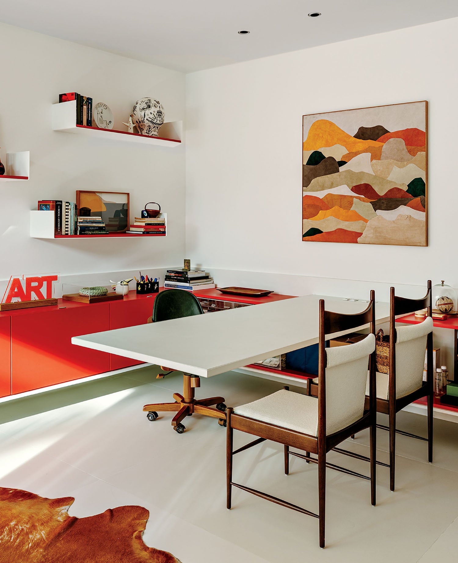 A white table with a red chair and a painting on the wall.