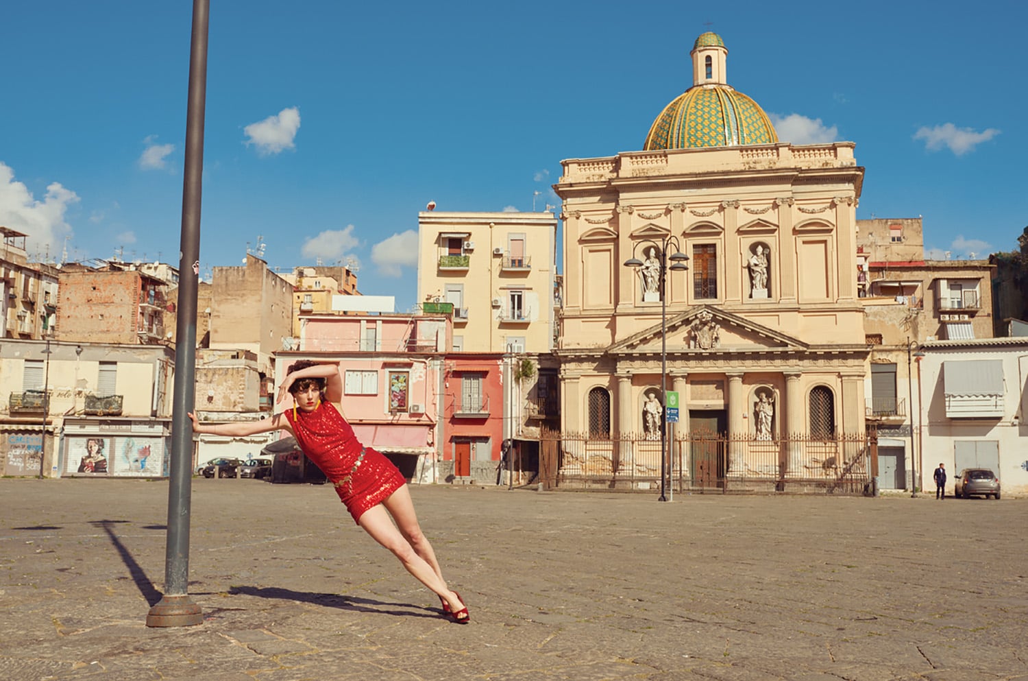 A woman in a red dress is leaning on a street sign.