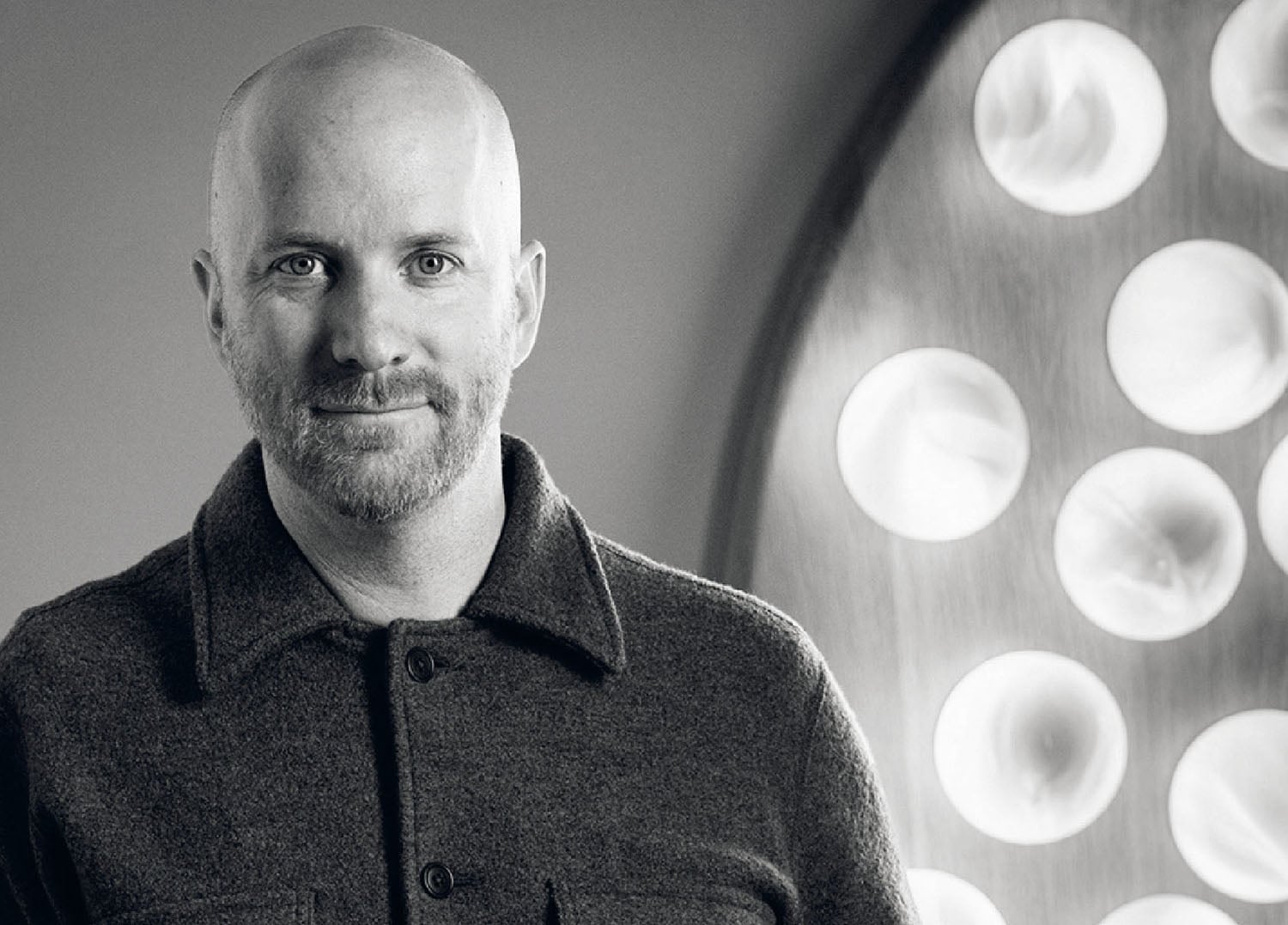 A man in a gray shirt standing in front of a clock.