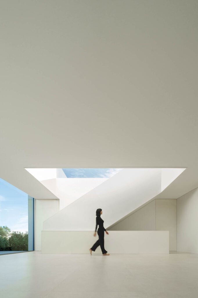 a woman walking through a minimalist patio under skylight