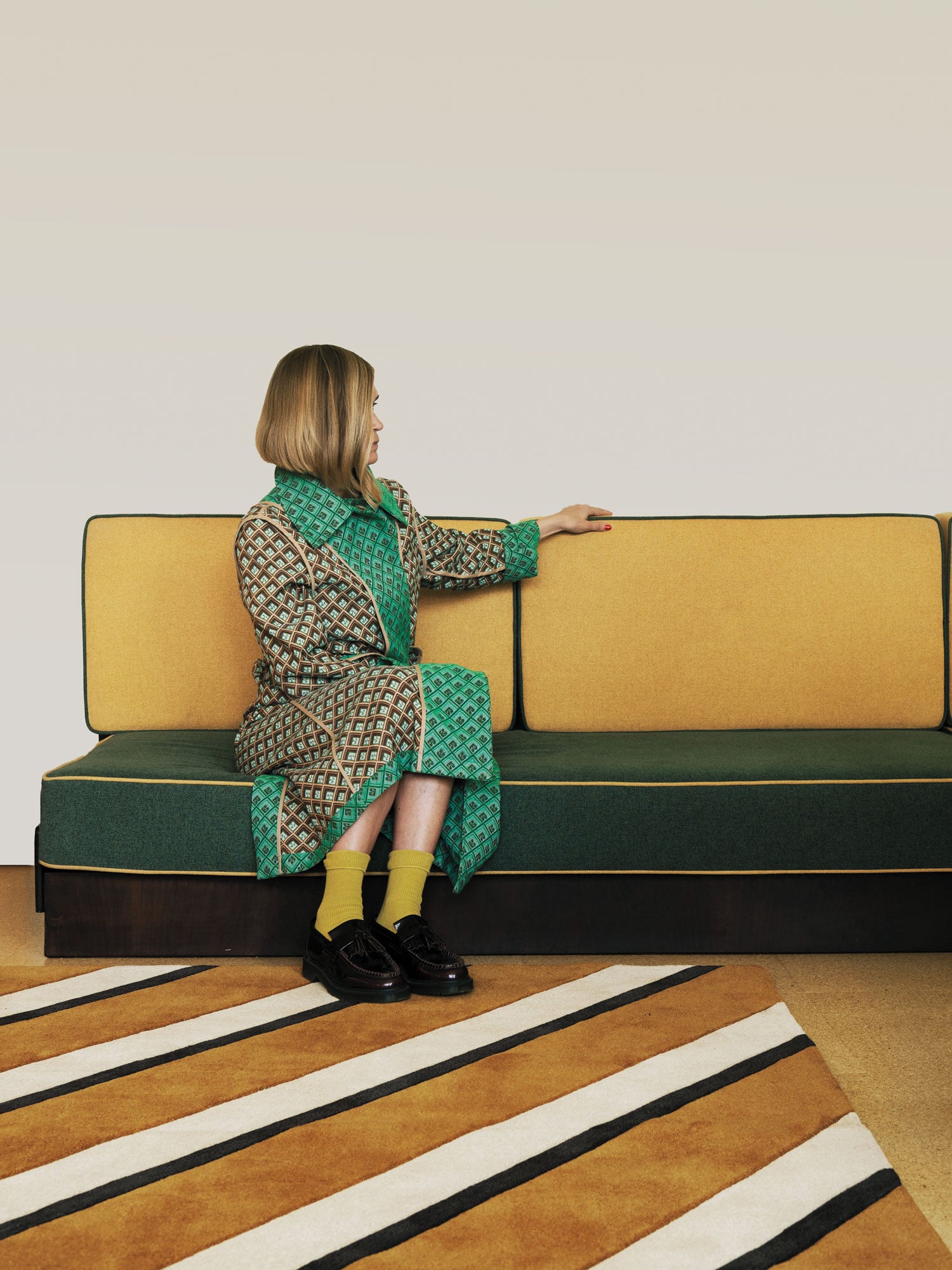 woman in green on yellow sofa atop brown and white striped rug