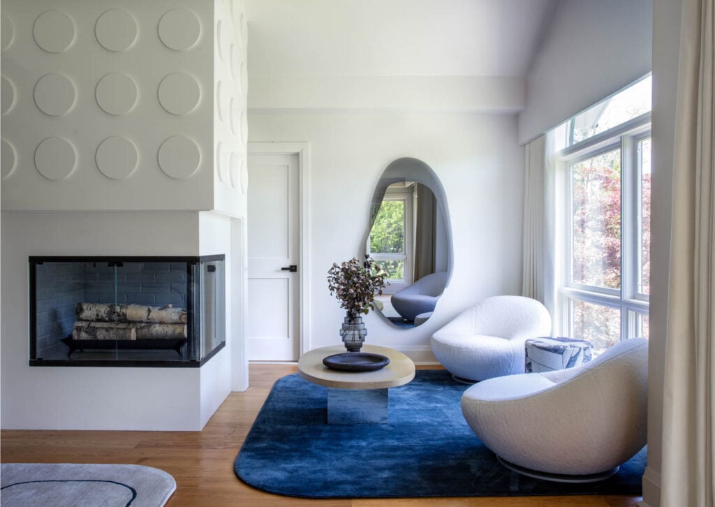 a white modern fireplace near two white chairs and blue rug